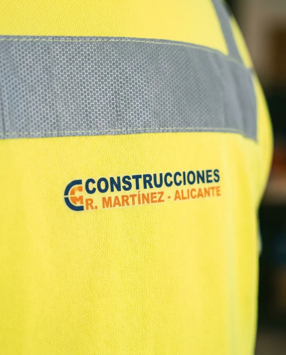 Detalle macro de transfer DTF aplicado en zona no reflectante de chaleco fluorescente de obra, bordes limpios sobre tejido amarillo