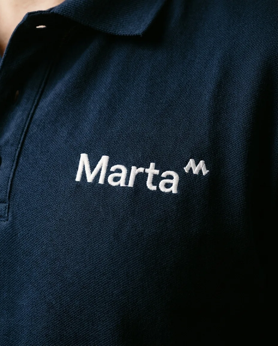 Detalle macro de bordado con nombre Marta en polo corporativo azul marino — personalización welcome pack empleados